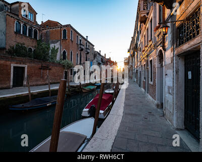 Venice Street & canal with boats moored up looking towards the setting sun Stock Photo