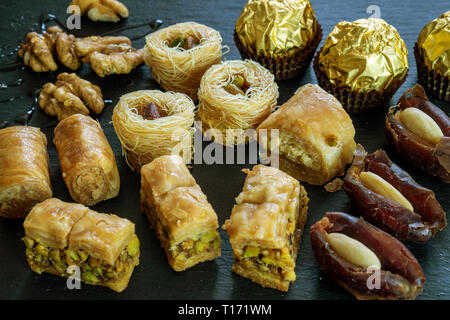 different type of arabian sweets background baklava borma nest ush-el-bul-bul asabi dates and chocolate on black stone background Stock Photo