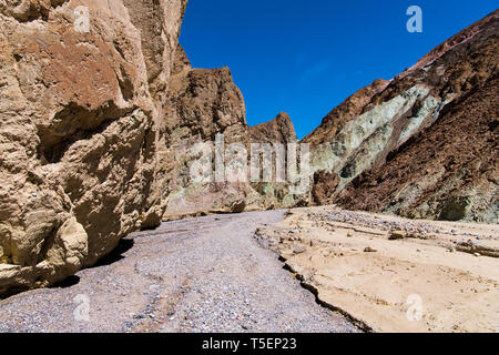 A dry riverbed of rocks and gravel curves through a canyon with colorful cliffs - Gower Gulch in Death Valley National Park Stock Photo