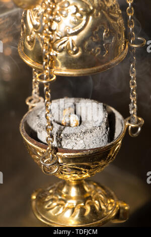 Worship service concept. Incense on burning coal tablet in golden censer emits fragrance smoke rising up. Close-up. Vertical photography with selectiv Stock Photo