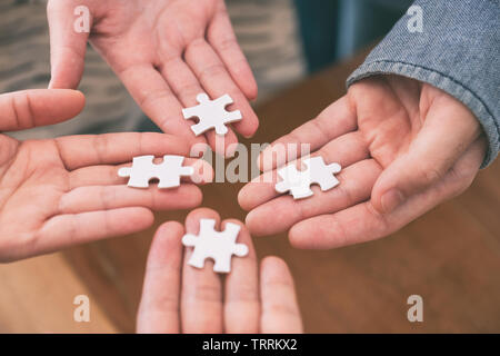 Closeup image of many people hands holding and putting a piece of white jigsaw puzzle together Stock Photo