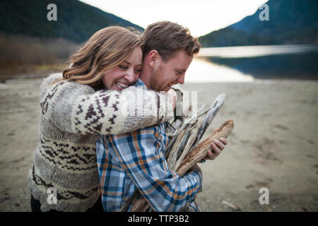 Cheerful girlfriend embracing boyfriend carrying firewood at Silver Lake Provincial Park Stock Photo