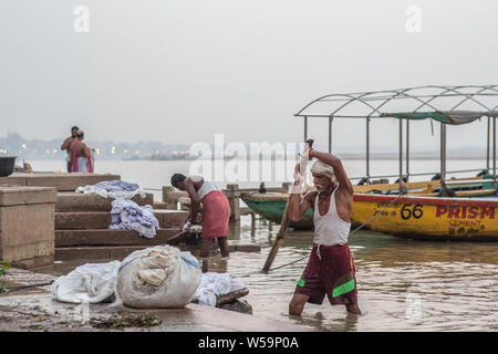 A man washing clothes in a traditional way with a large stick in the Ganges river in Varanasi. Stock Photo