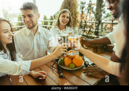 Young group of friends drinking beer, having fun, laughting and celebrating together. Women and men with beer's glasses in sunny day. Oktoberfest, friendship, togetherness, happiness, summer concept. Stock Photo