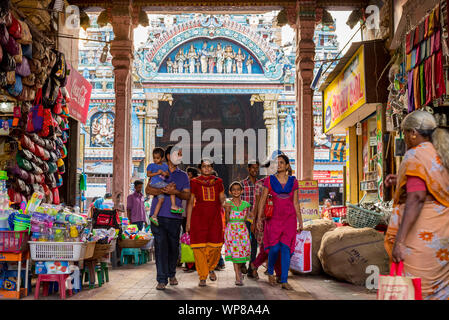 Madurai, Tamil Nadu / India - January 14, 2016: an Indian family walks through an arch occupied by shops, with famous Meenakshi Temple behind. Stock Photo