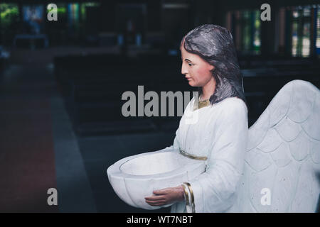 Angel statue holding bowl of holy water at the Church's entrance. Selective focus. Copy space. Stock Photo