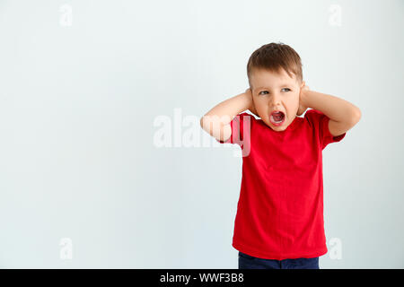 Screaming little boy with autistic disorder covering ears on light background Stock Photo