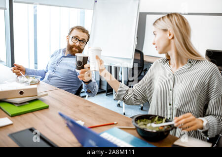 Mann und Frau Salat und Kaffee trinken während einer Mittagspause am Arbeitsplatz ohne das Büro zu verlassen Stockfoto