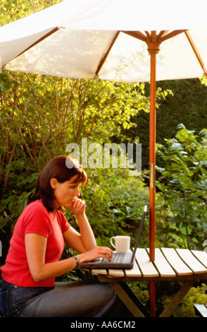 Donna al lavoro su computer portatile a casa in giardino Foto Stock