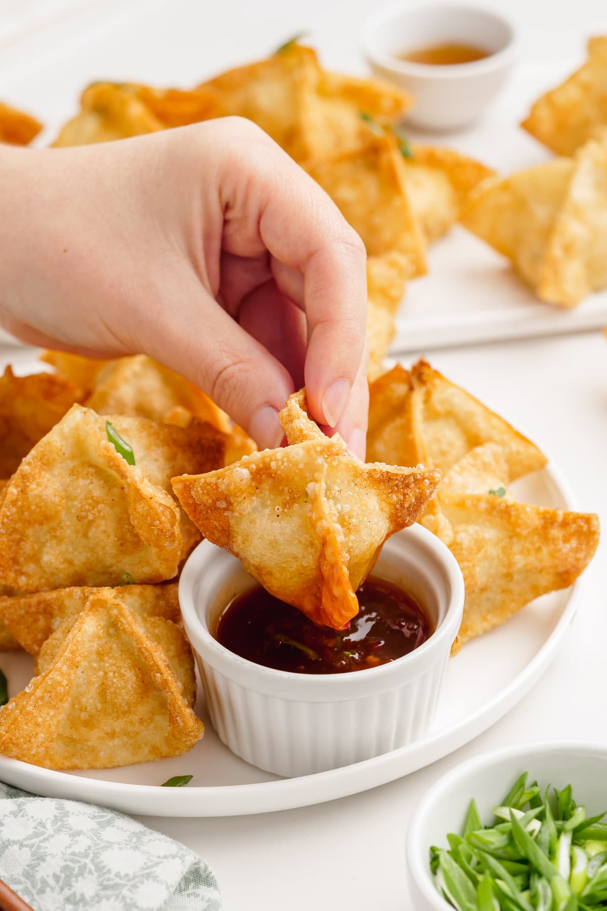 woman's hand dipping a crab rangoon in sauce