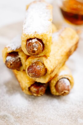 A stack of breakfast pigs in a blanket with powdered sugar on a plate.