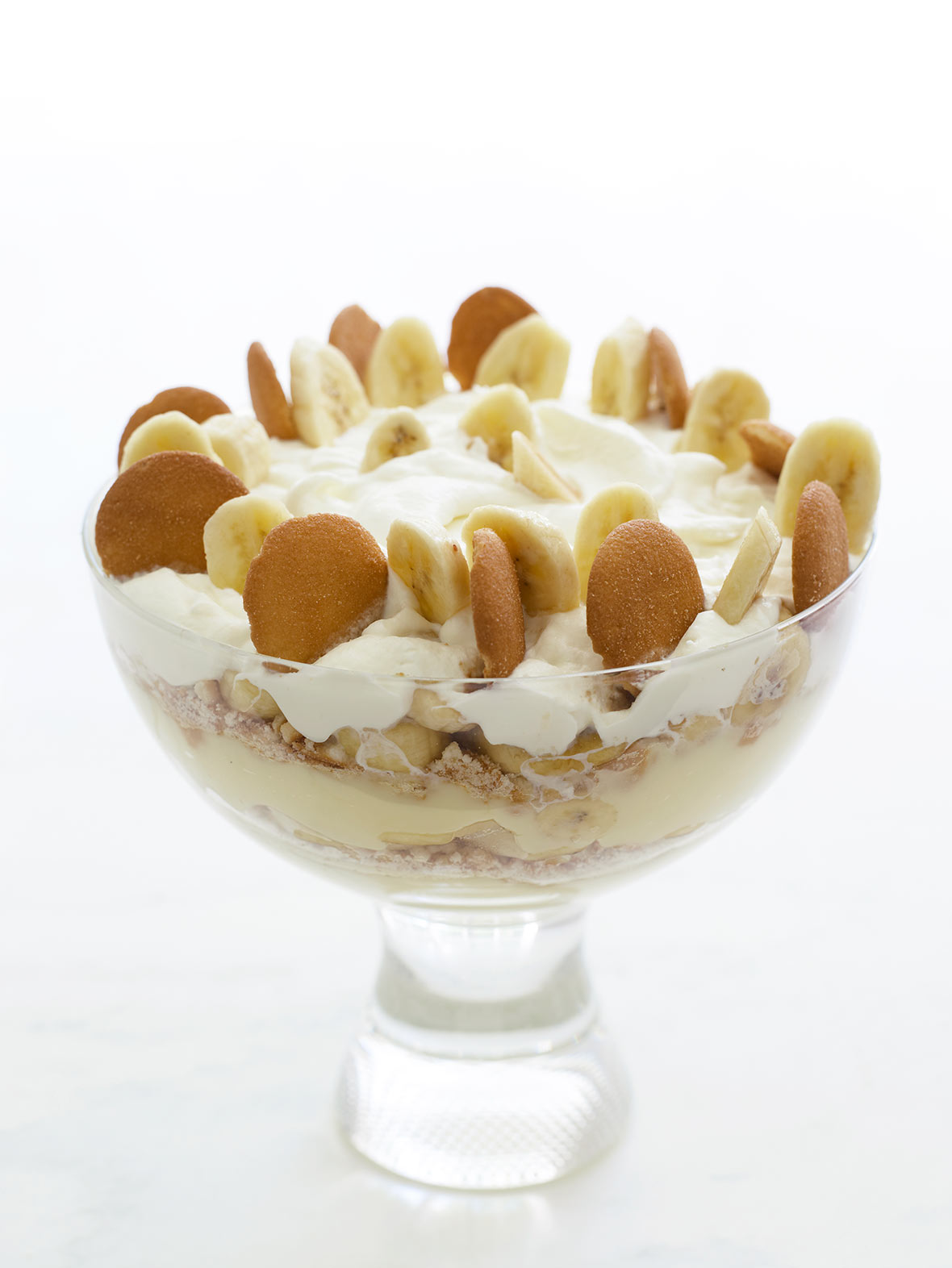 Big glass bowl of layers of vanilla wafer banana pudding topped with sliced bananas, Nilla wafers, and whipped cream