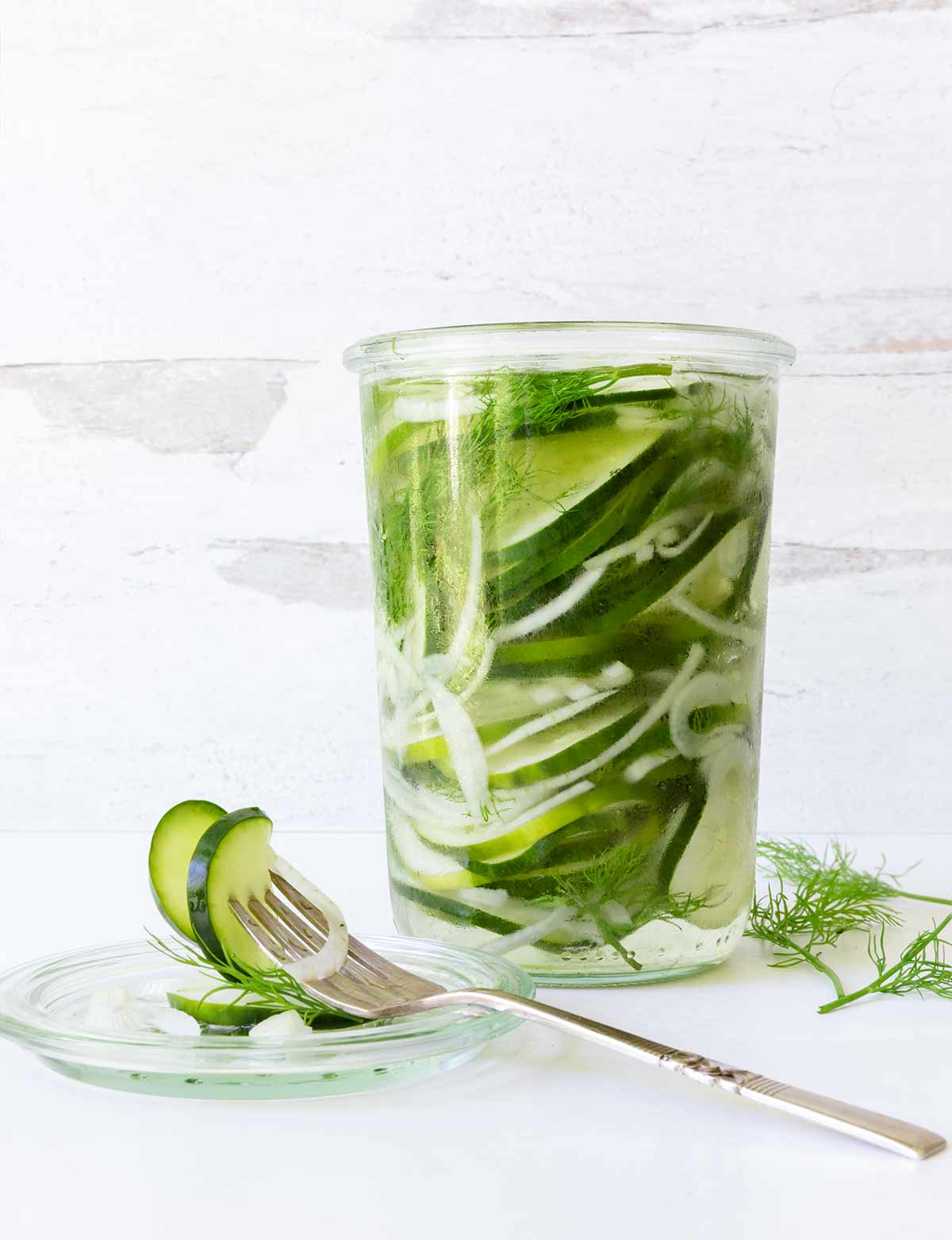 A jar of refrigerator sweet pickles with a fork holding two pickles lying beside the jar.