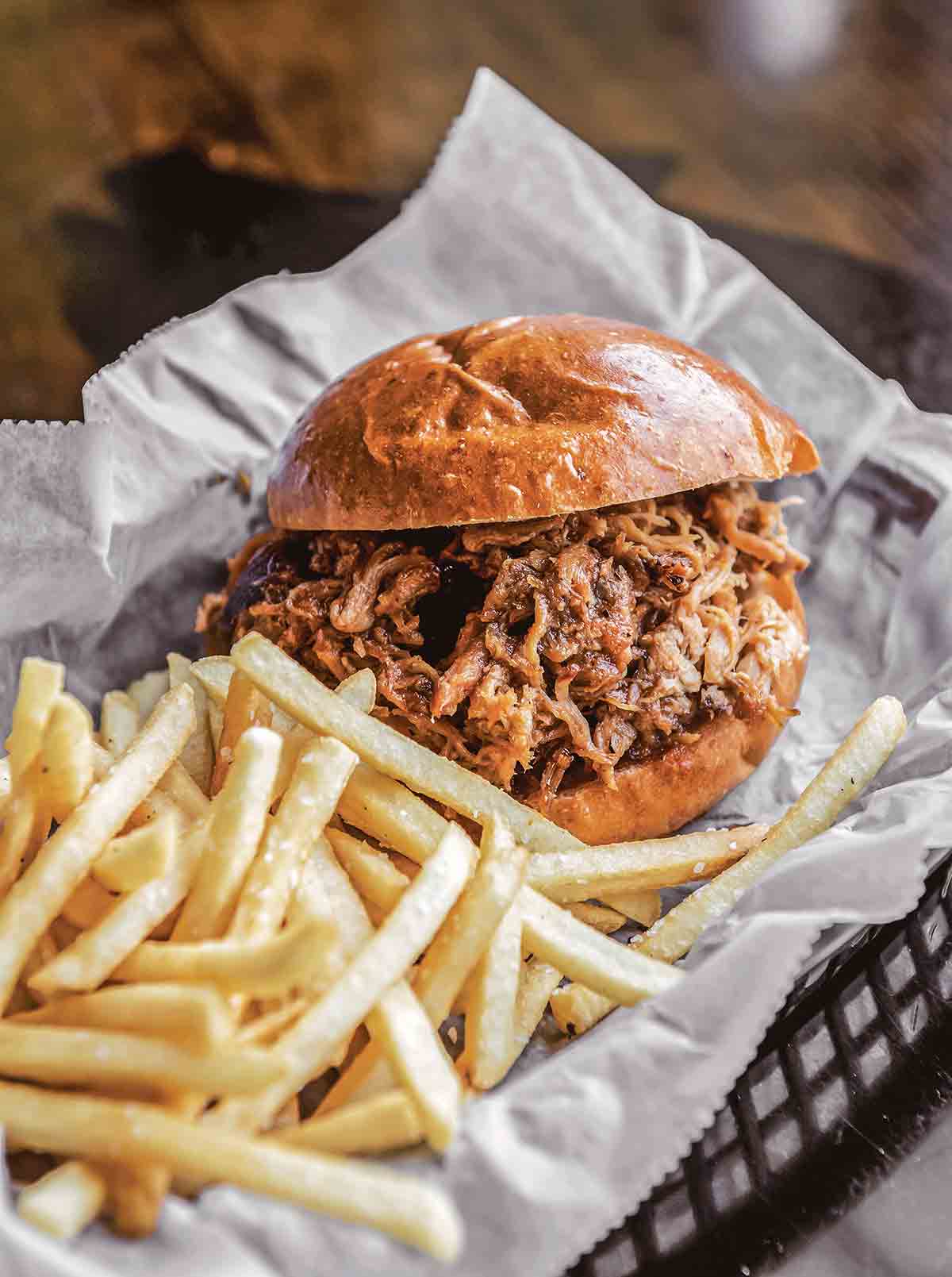 A smoked chicken sandwich and fries in a plastic basket lined with paper.