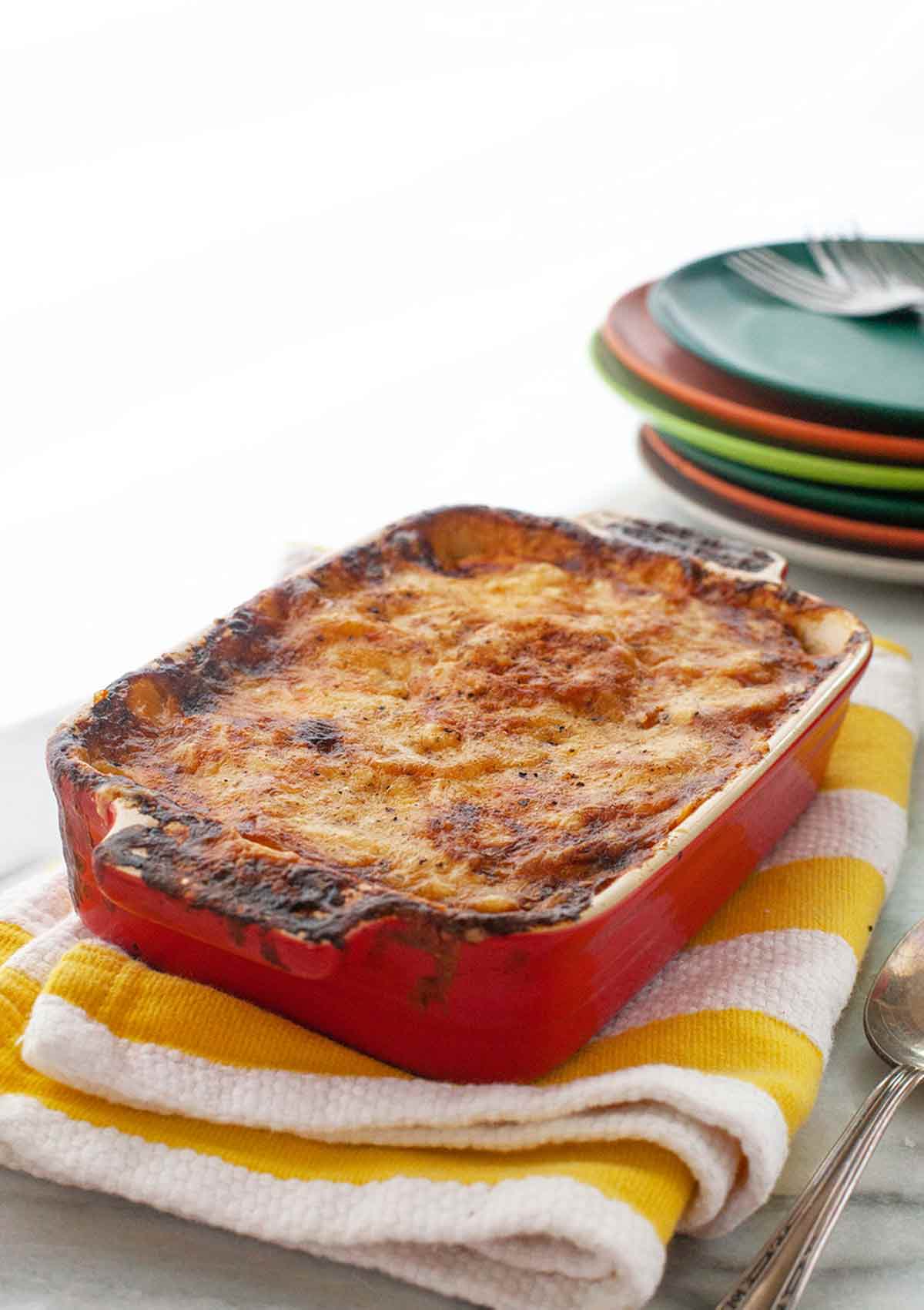 A ham, cheese, and potato casserole in a large rectangular dish, on a red-and-white striped towel.