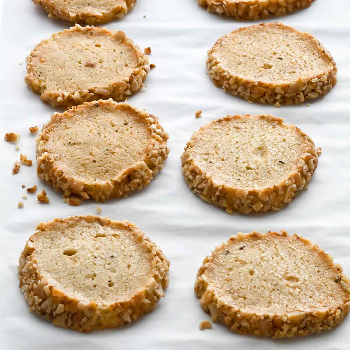 Ten Stilton and walnut crackers arranged in rows on a sheet of parchment.