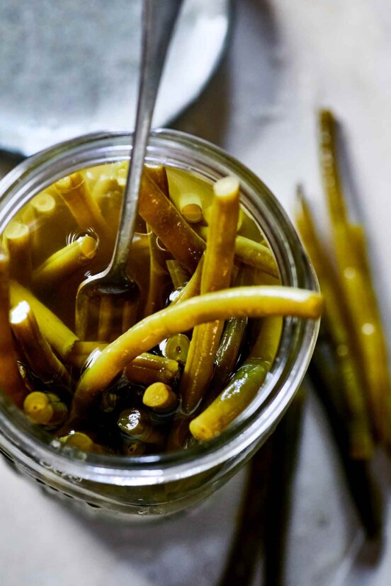 Close-up looking into a mason jar full of pickled green beans and pickling liquid, with a fork.