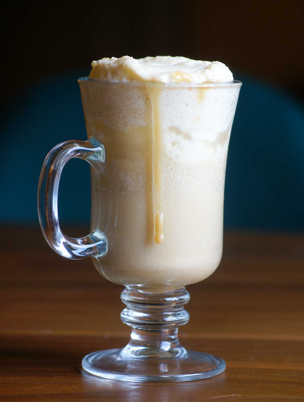 An Irish coffee mug filled with butterscotch beer with foam on top and a drizzle of butterscotch sauce.