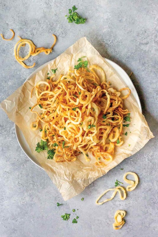 Dairy-free crispy onion strings on a sheet of parchment, on a white plate, garnished with parsley.