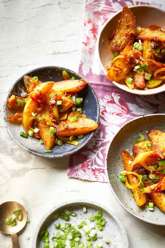 Tareko aloo in three bowls, garnished with rings of scallion.