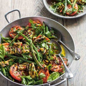 A large and small bowl filled with grilled vegetables salad and two serving spoons in the large bowl.