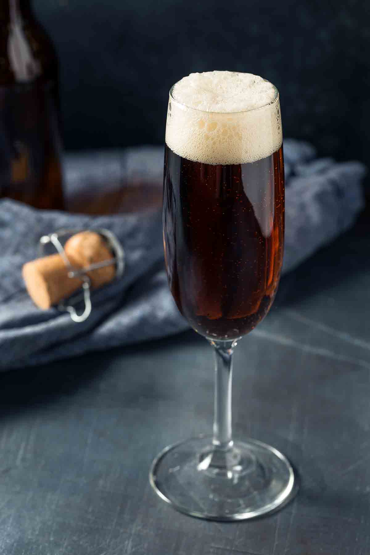 A black velvet cocktail in a flute with a napkin and cork in the background.