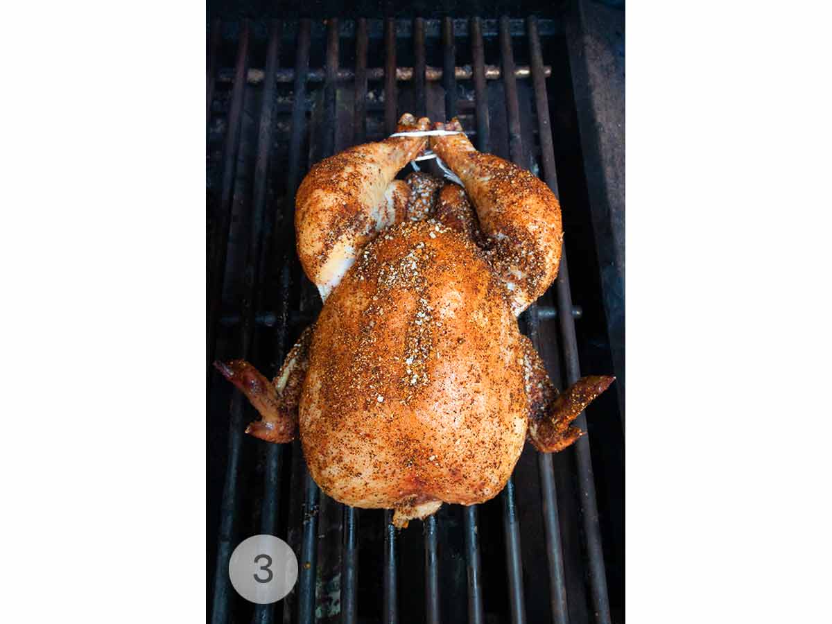 A spice-rubbed whole chicken being smoked on a grill.