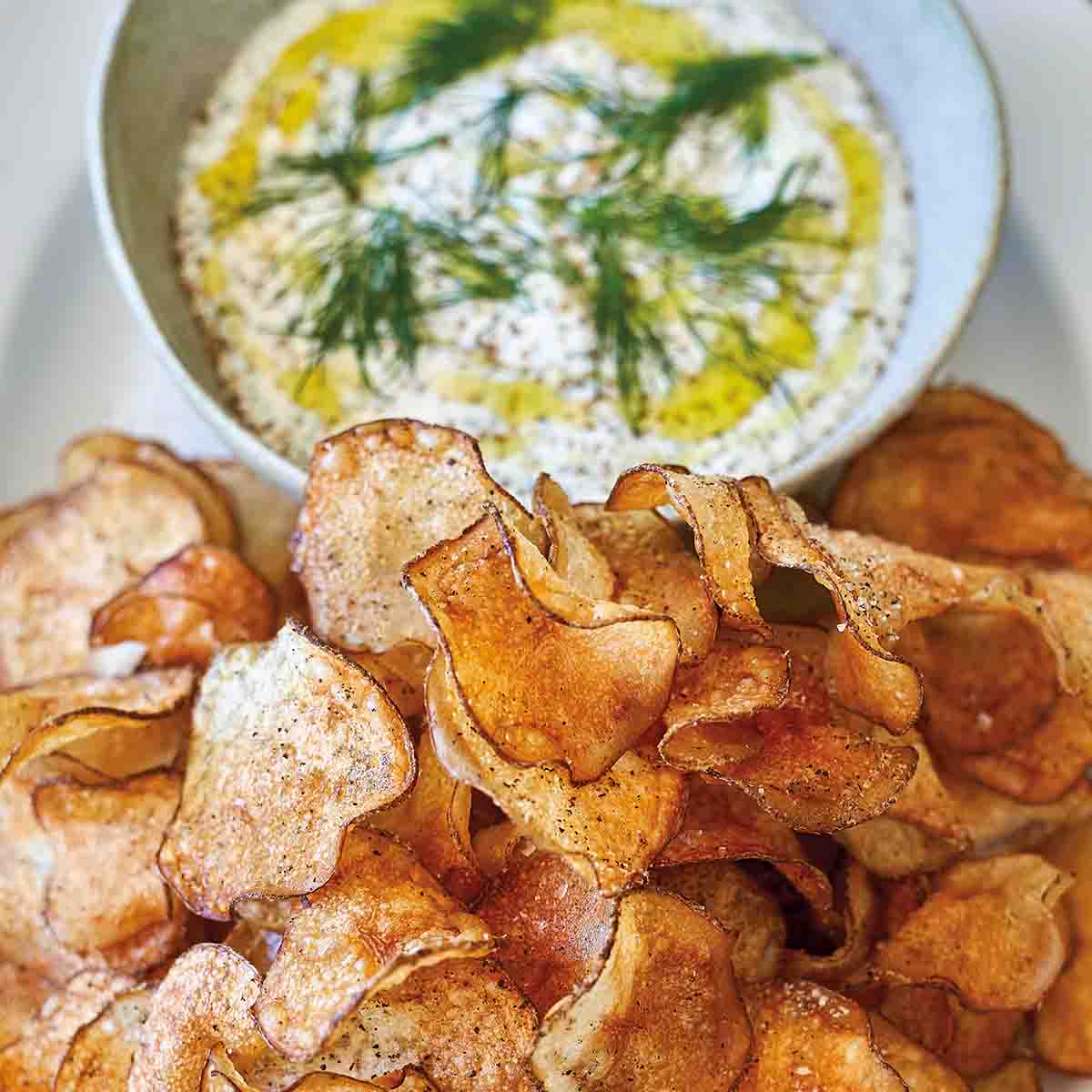 A white oval platter holding a bowl of dill dip with potato chips beside it.