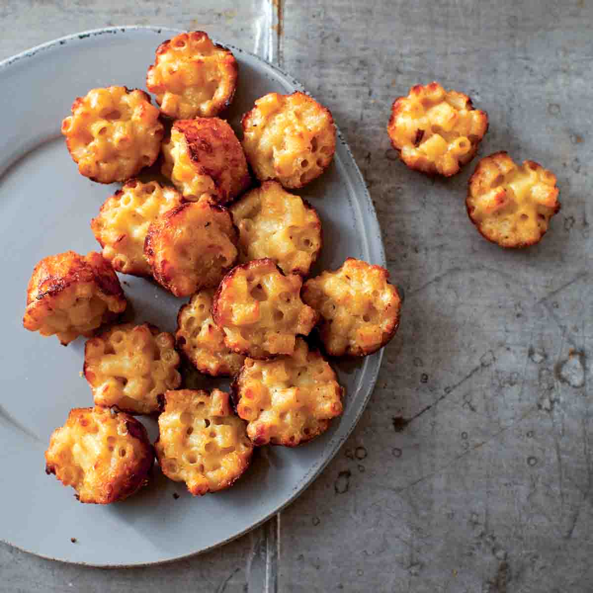 A grey plate half-filled with mac and cheese canapes, with a few resting beside the plate.