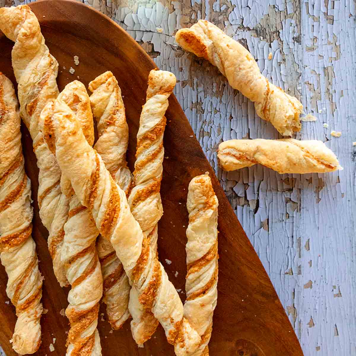 Cheese straws on an oval wooden platter on a distressed wooden surface.