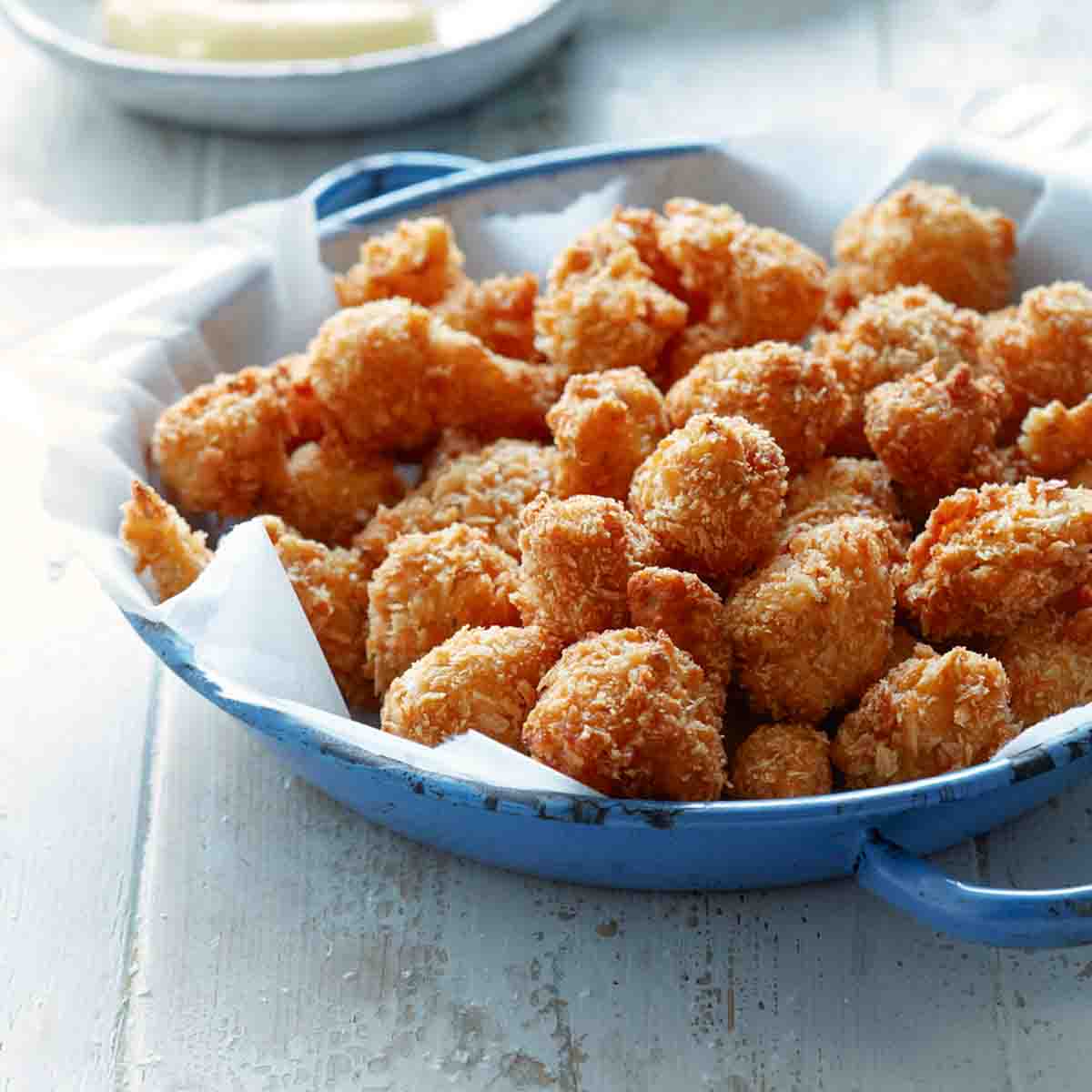 A blue skillet with paper towel and a pile of breaded, deep-fried cauliflower. A bowl of dip in the background.