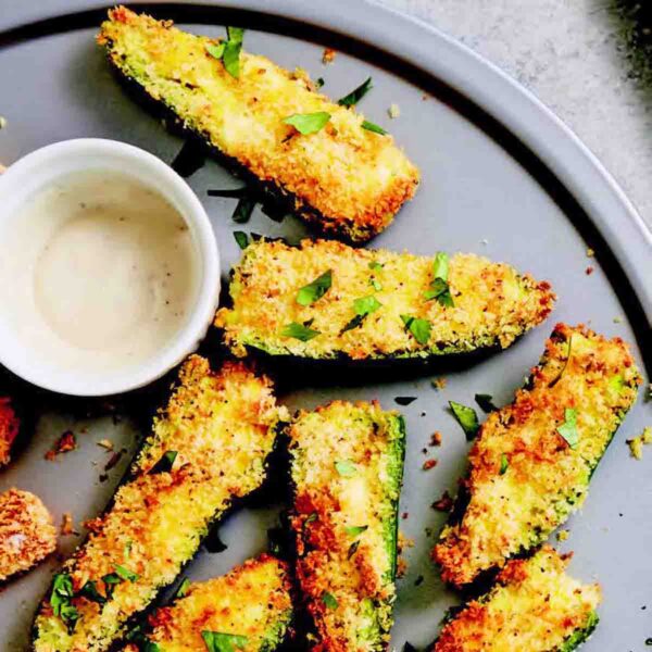 A grey plate filled with jalapeño popper halves and a bowl of white dip on the side.