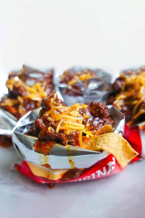 Chili and grated cheddar on top of Fritos in open mini bags of Fritos.