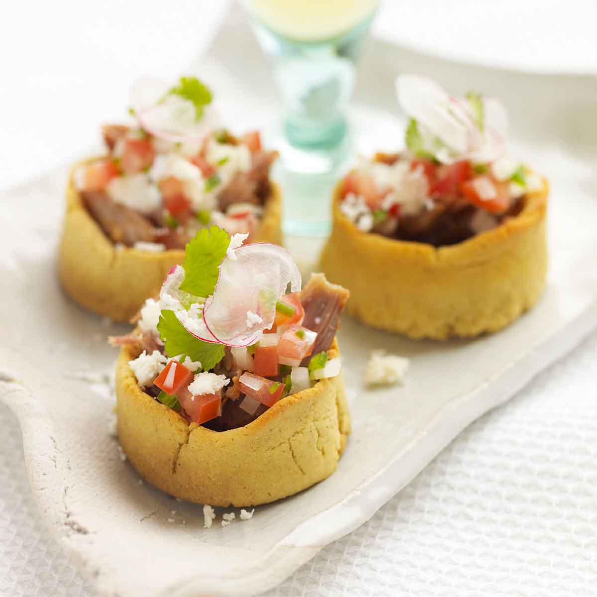 Three Mexican sopes on a rustic platter with a glass of white wine in the background.