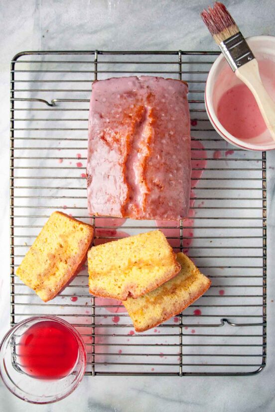 A blood orange pound cake on a wire rack with glaze and sugar syrup, three slices cut.