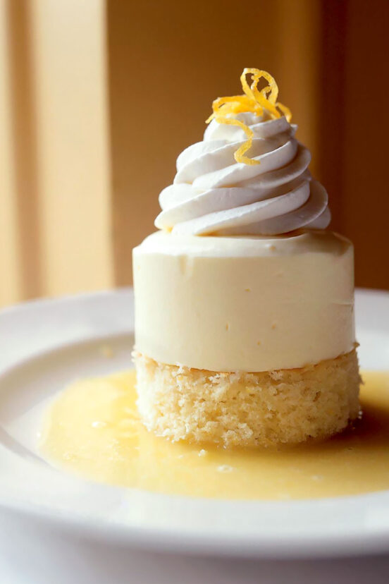 Lemon semifreddo in a pool of lemon sauce and garnished with a twist of lemon, sitting on a white dessert plate.