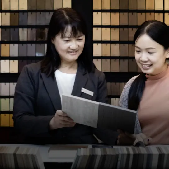 Two women looking at 2 wooden laminate samples against a wall of laminate colours collection