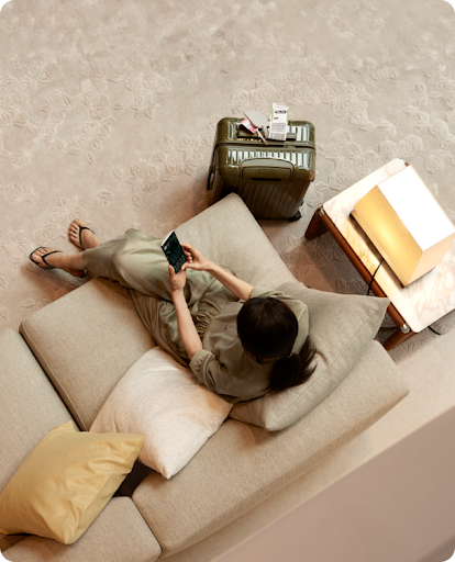 Woman sitting on couch adjusting her thermostat with google home product from her mobile device