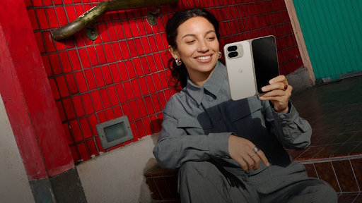 A smiling woman sits in a chair, looking at an open fold phone in her hand.