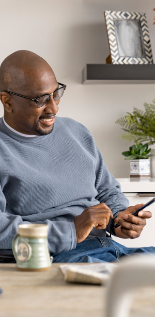 A man in a wheelchair looking at his android phone sitting by a dining table.