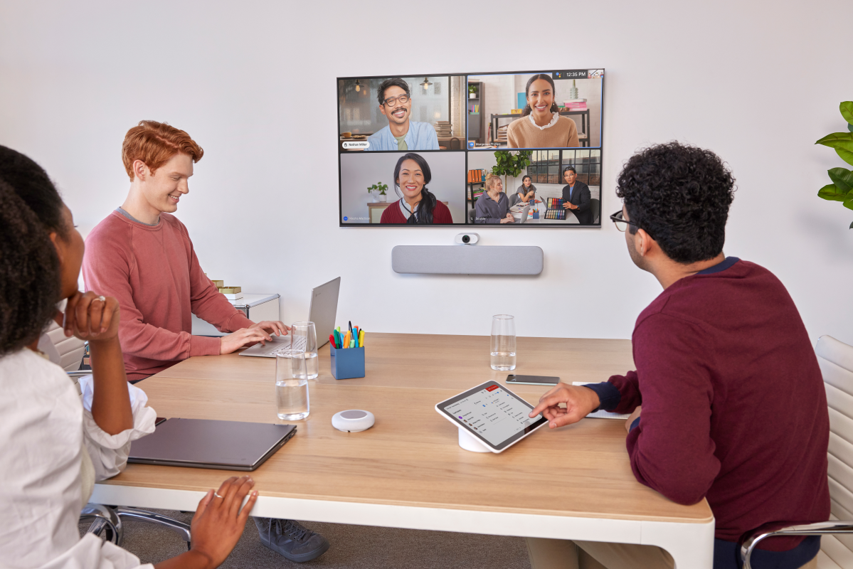 Una sala riunioni con tre persone e altre quattro visualizzate sullo schermo in videoconferenza