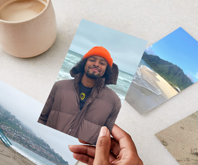 A hand holding a photo print of a man in jacket and orange winter hat.