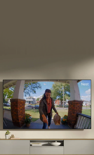 A TV in a living room showing a delivery person standing on a stoop waving to the doorbell camera.