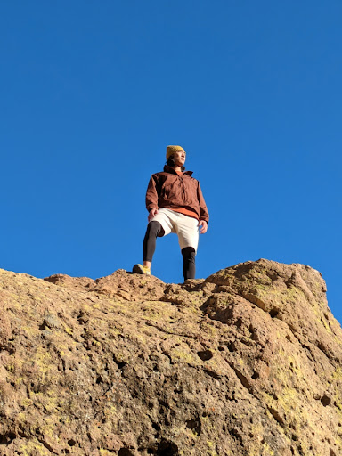 We see a person enjoying a view of the clear blue sky while on a hike.