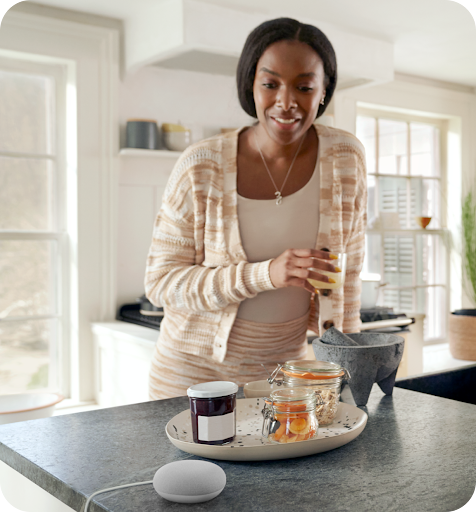 Women drinking juice in her kitchen looking at her google home device