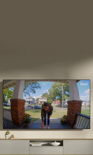 Un écran de télévision installé dans un salon montrant une livreuse sur le perron qui fait signe à la sonnette vidéo.