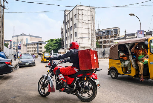 person on motorbike with a red health package attached to the back of the bike