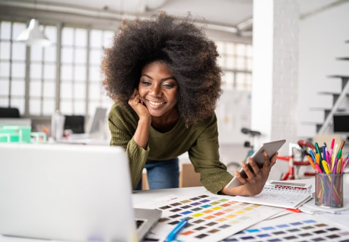 Une femme dans un bureau regardant son ordinateur, une tablette à la main 