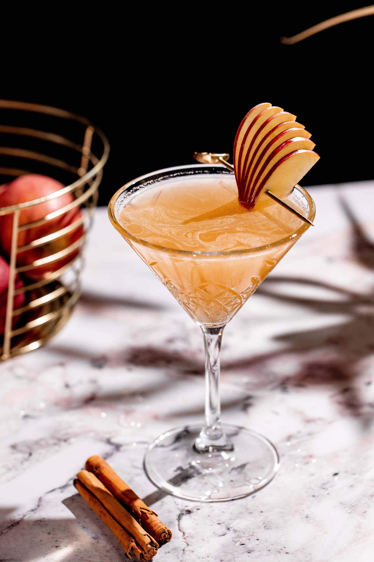 An apple cider martini with slices of an apple for garnish on the rim of the glass. 