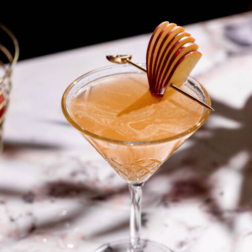 Apple cider martini in a cocktail glass on a white table with an apple garnish.